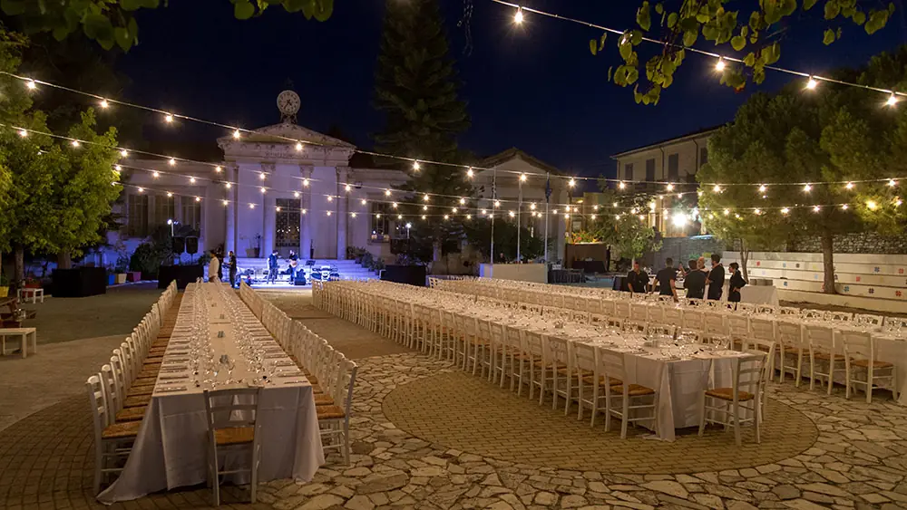 Long banquet tables under string lights in a village square for a traditional Greek fiesta